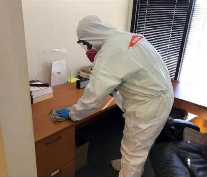 SERVPRO technician in full personal protective equipment disinfecting surfaces in a commercial building 